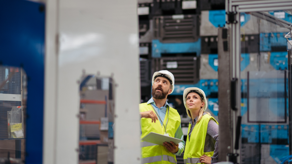 Two engineers in hard hats and safety vests inspecting industrial control systems on a plant floor