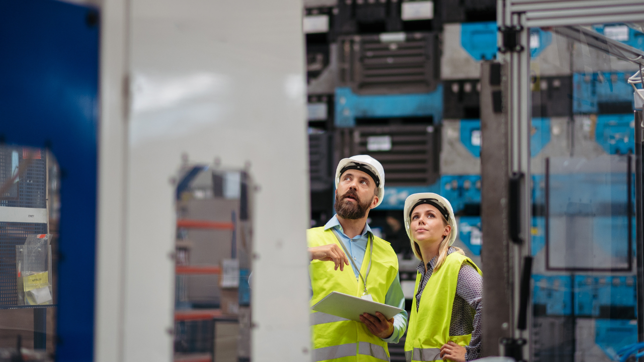 Two engineers in hard hats and safety vests inspecting industrial control systems on a plant floor