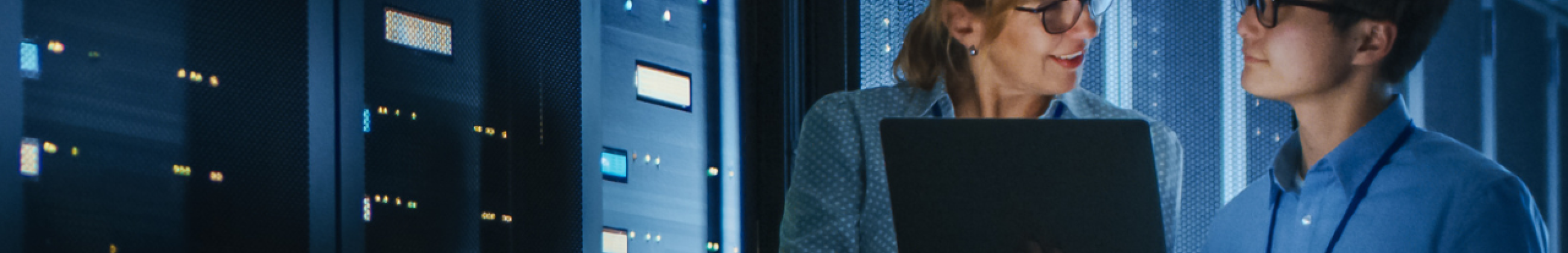 Two IT and OT security engineers reviewing system data on laptop in server room representing cross-functional NIST cybersecurity framework collaboration
