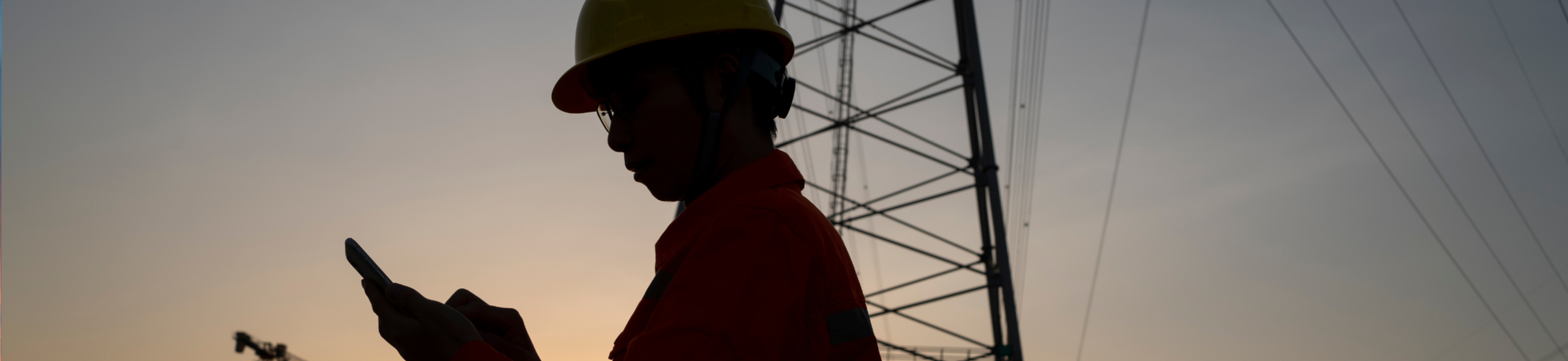 Energy sector field engineer reviewing data on tablet at transmission tower site at dusk representing operational decision-making gap between NERC CIP compliance and OT security