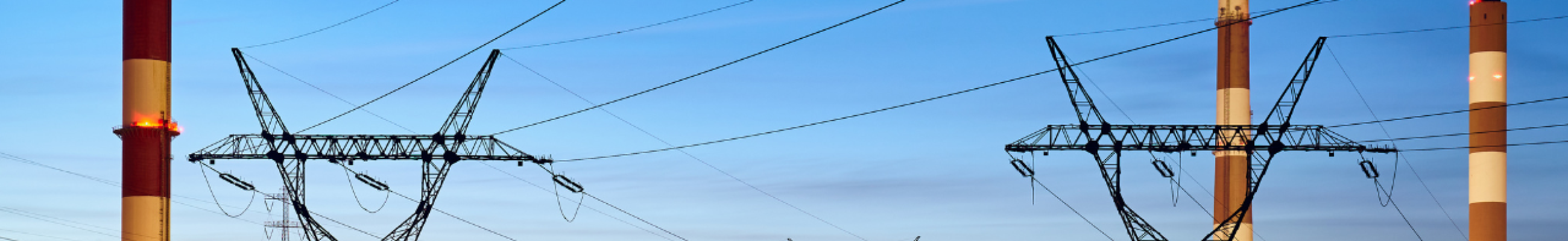 Power generation facility at dusk with high-voltage electricity transmission towers, industrial chimneys, and lit infrastructure representing OT critical infrastructure security risks.
