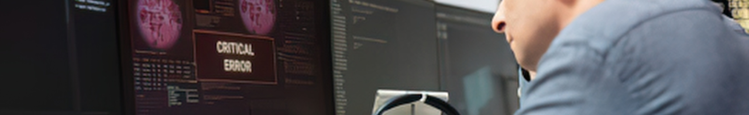 OT cybersecurity analyst monitoring dual screens displaying a critical error alert on an industrial control system, representing an active OT security incident response scenario.