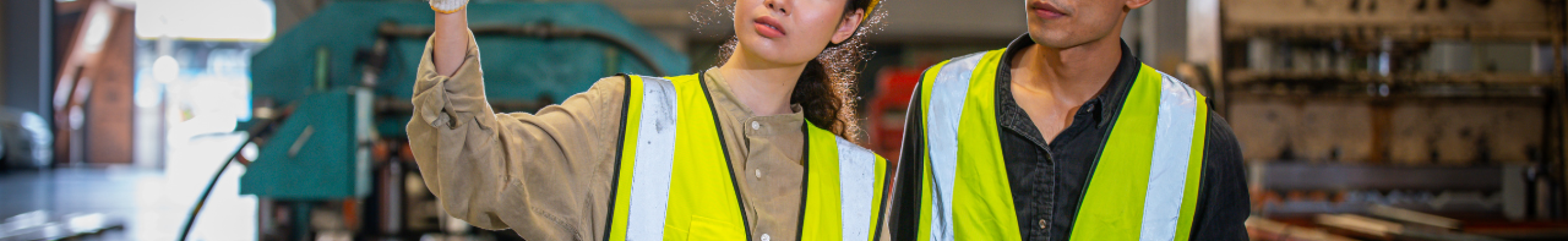 Two plant workers in hard hats and safety vests communicating on a manufacturing floor